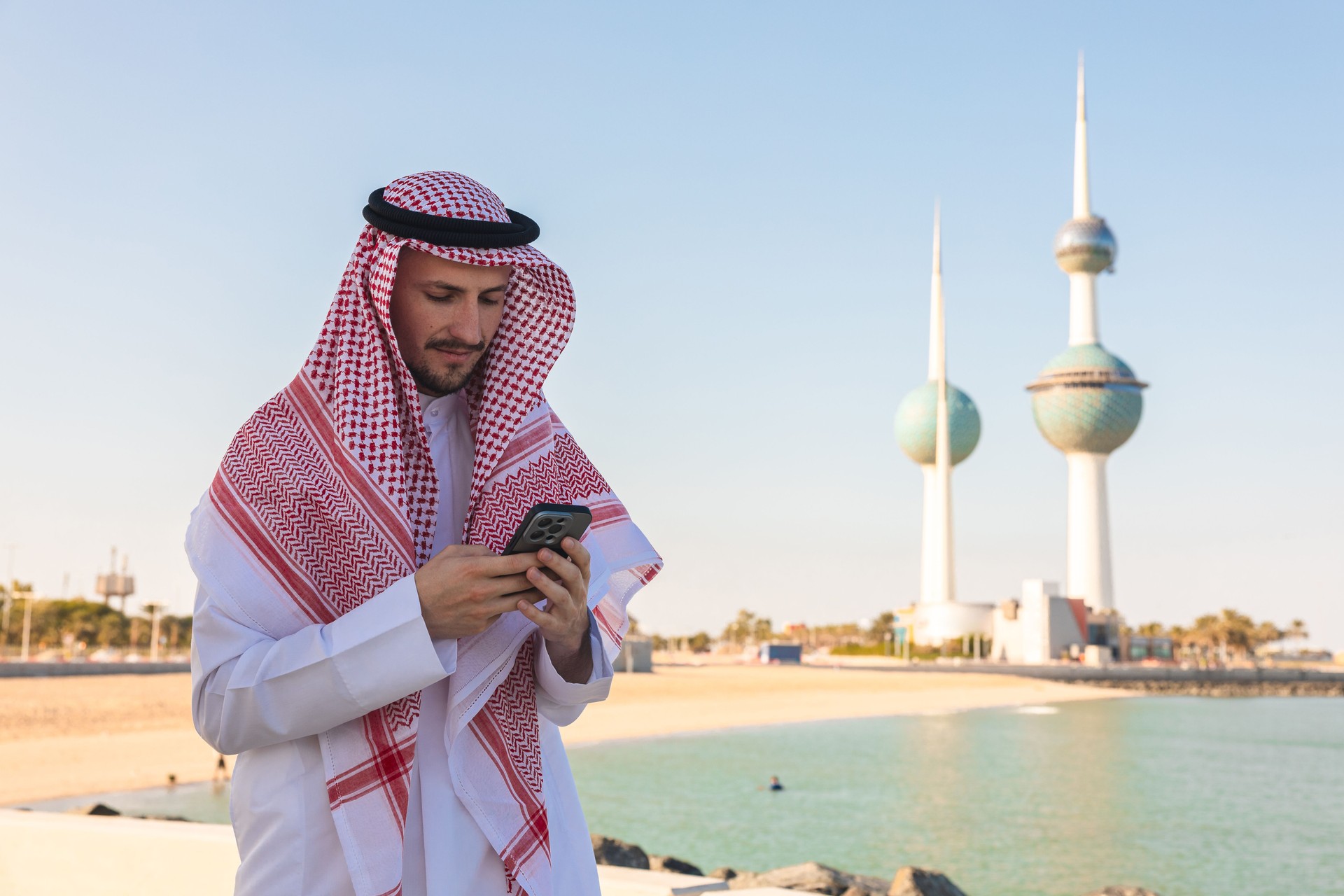 Young man wearing traditional clothing in Kuwait using his phone outdoors